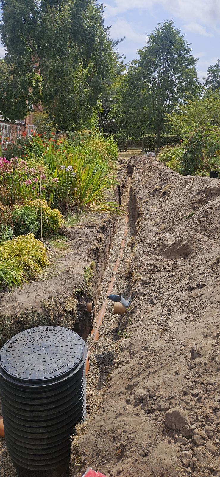 Treatment plant chamber riser and orange pipe laid in a garden trench